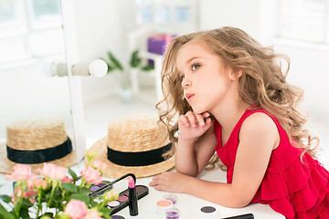 Image showing A little girl with cosmetics. She is in mother\'s bedroom, sitting near the mirror.