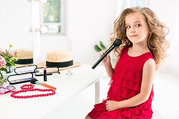 Image showing A little girl with cosmetics. She is in mother\'s bedroom, sitting near the mirror.