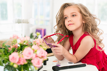 Image showing A little girl with cosmetics. She is in mother\'s bedroom, sitting near the mirror.