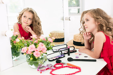 Image showing A little girl with cosmetics. She is in mother\'s bedroom, sitting near the mirror.