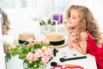 Image showing A little girl with cosmetics. She is in mother\'s bedroom, sitting near the mirror.