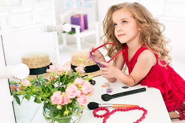 Image showing A little girl with cosmetics. She is in mother\'s bedroom, sitting near the mirror.