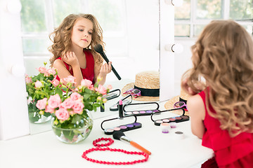 Image showing A little girl with cosmetics. She is in mother\'s bedroom, sitting near the mirror.