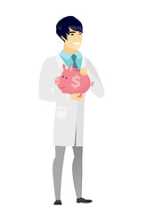 Image showing Asian doctor holding a piggy bank.