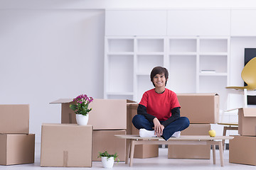 Image showing boy sitting on the table with cardboard boxes around him