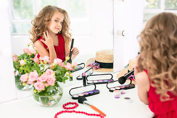 Image showing A little girl with cosmetics. She is in mother\'s bedroom, sitting near the mirror.