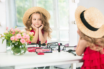 Image showing A little girl with cosmetics. She is in mother\'s bedroom, sitting near the mirror.