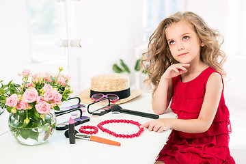 Image showing A little girl with cosmetics. She is in mother\'s bedroom, sitting near the mirror.