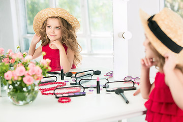 Image showing A little girl with cosmetics. She is in mother\'s bedroom, sitting near the mirror.