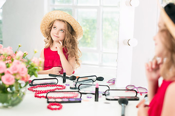 Image showing A little girl with cosmetics. She is in mother\'s bedroom, sitting near the mirror.