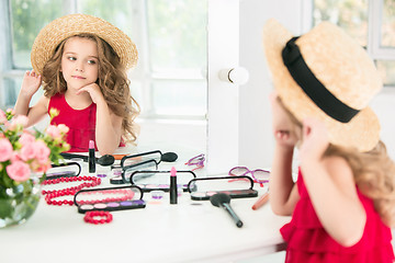 Image showing A little girl with cosmetics. She is in mother\'s bedroom, sitting near the mirror.