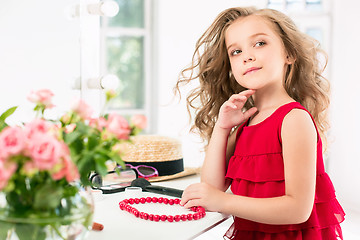 Image showing A little girl with cosmetics. She is in mother\'s bedroom, sitting near the mirror.