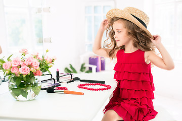 Image showing A little girl with cosmetics. She is in mother\'s bedroom, sitting near the mirror.