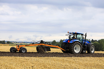 Image showing Farmer Works With New Holland Tractor and Leveller