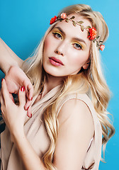 Image showing young pretty blond girl with curly blond hair and little lowers happy smiling on blue sky background, lifestyle people concept 