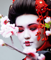 Image showing young pretty geisha in black kimono among sakura, asian ethno close up