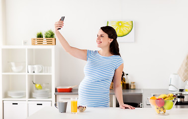 Image showing happy pregnant woman with smartphone at kitchen