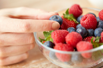 Image showing close up of young woman hand with berries in bowl