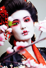 Image showing young pretty geisha in kimono with sakura and red decoration design on white background