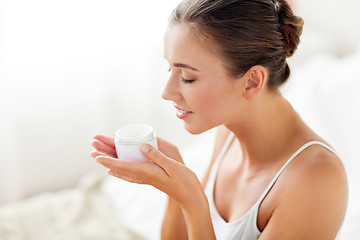 Image showing close up of happy woman holding and smelling cream