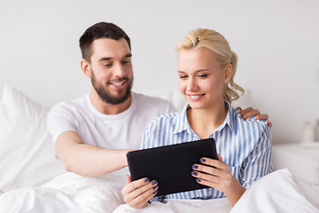 Image showing smiling happy couple with tablet pc in bed at home