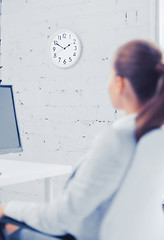 Image showing businesswoman looking at wall clock in office