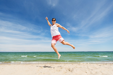Image showing smiling young man jumping on summer beach