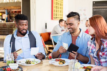 Image showing happy friends paying bill for food at restaurant