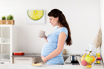 Image showing happy pregnant woman with mug and cake at home
