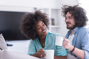 Image showing multiethnic couple sitting on sofa at home drinking coffe