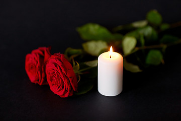 Image showing red roses and burning candle over black background