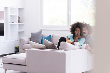 Image showing multiethnic couple sitting on sofa at home drinking coffe