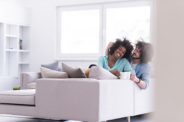 Image showing multiethnic couple sitting on sofa at home drinking coffe