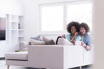 Image showing multiethnic couple sitting on sofa at home drinking coffe