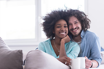 Image showing multiethnic couple sitting on sofa at home drinking coffe