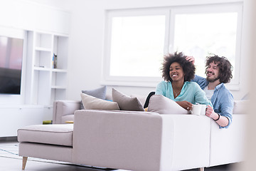 Image showing multiethnic couple sitting on sofa at home drinking coffe