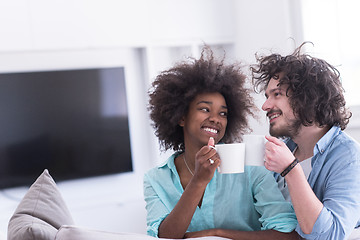 Image showing multiethnic couple sitting on sofa at home drinking coffe