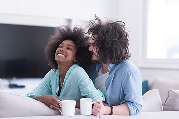 Image showing multiethnic couple sitting on sofa at home drinking coffe