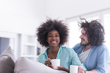 Image showing multiethnic couple sitting on sofa at home drinking coffe