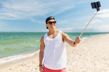 Image showing man with smartphone selfie stick on summer beach