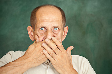 Image showing Shocked senior gentleman holding his hand against his mouth and looking at the camera