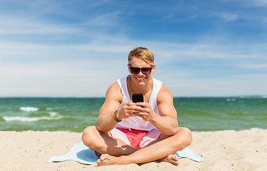 Image showing happy smiling young man with smartphone on beach