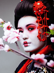 Image showing young pretty geisha in black kimono among sakura, asian ethno close up