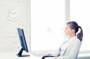 Image showing businesswoman looking at wall clock in office