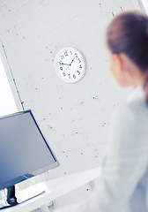 Image showing businesswoman looking at wall clock in office