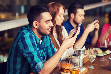 Image showing friends with smartphones dining at restaurant