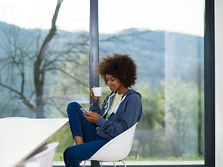 Image showing black woman drinking coffee and using a mobile phone  at home