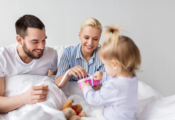 Image showing happy family with gift box in bed at home