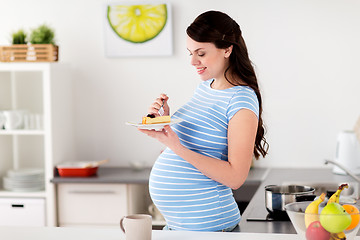 Image showing happy pregnant woman eating cake at home kitchen