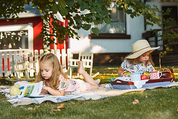 Image showing Cute Little Blond Girls Reading Book Outside on Grass